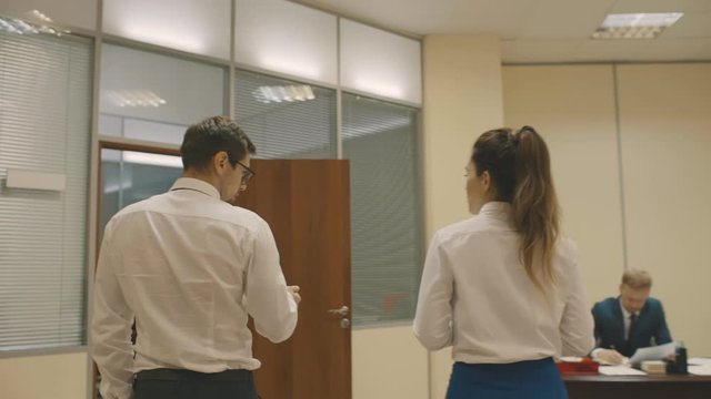 Close up of back view of young modern businessman with his female colleague talking and walking through the office room and coming to their workplace at start up company