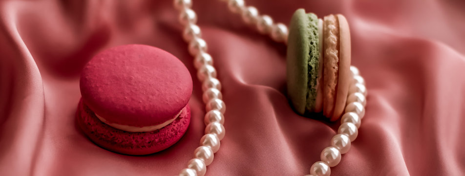 Sweet macaroons and pearls jewellery on silk background, parisian chic jewelry, French dessert food and cake macaron for luxury confectionery brand, holiday gift