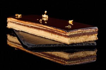A slice of puff cake with chocolate icing. Black background. Close-up.