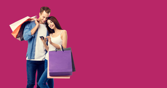 Love, holiday sales, shop, retail, consumer concept - happy couple with shopping bags, looking at mobile phone, standing close to each other. Over red color background.