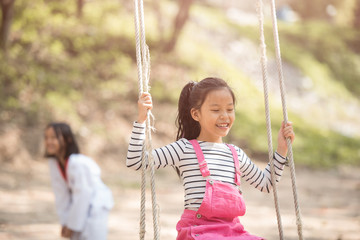happy little asian girl child having fun to playing in the playground in summer time with smile and laughing healthy, Adorable girl having fun on a swing on summer. happy vacation lifestyle concept.