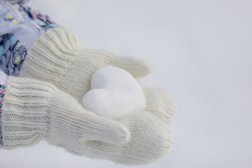 Valentine day background. Female hands in knitted mittens with heart of snow in winter day. Love concept. 