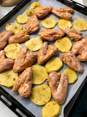 Homemade Marinated Raw Chicken Wings with Sliced Potato Slices and Sauce on Baking Tray with Oven Sheet Paper Ready to Bake.