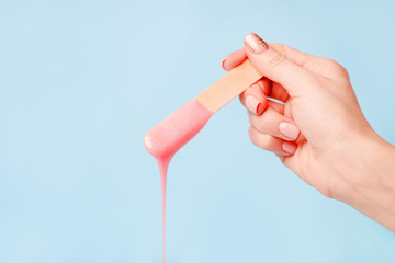 liquid pink pearl wax or sugar paste for depilation drains from the stick on blue background. The...