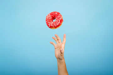 Hand catch a donut with red icing. Blue cardboard background. The concept of baking, handmade. Flat...