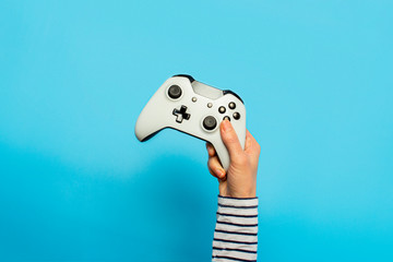 Female hand hold a gamepad on a blue background. Concept of the game, e-sports, leisure, gaming...