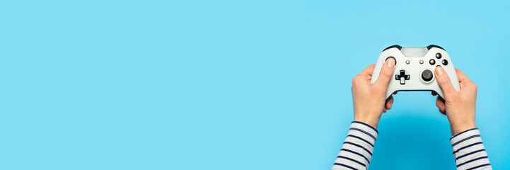 Female hands hold a gamepad on a blue background. Concept of the game, e-sports, leisure, gaming industry, video games. Banner. Flat lay, top view © Alex