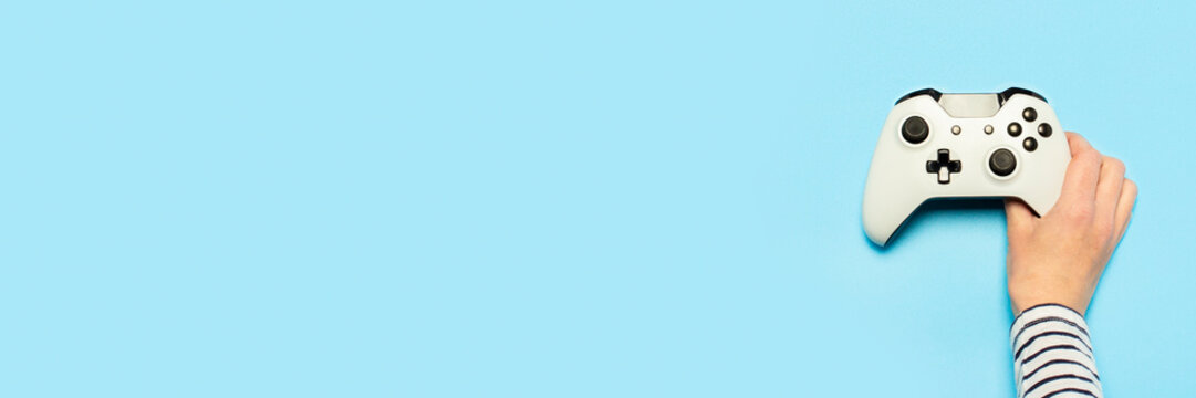 Female hand hold a gamepad on a blue background. Concept of the game, e-sports, leisure, gaming industry, video games. Banner. Flat lay, top view