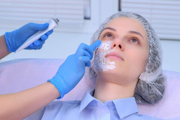 Cosmetologist is applying cream with anesthesia on patient's face, portrait closeup view. Preparing...