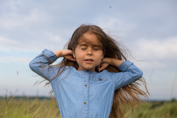 horizontal photo six year old girl with long hair fluttering in the wind stands with her eyes closed