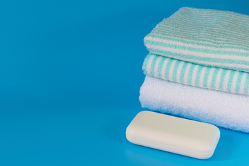 Soft and fluffy towels on a blue background. Soap for bath, laundry and body care. Personal hygiene products. Bath amenities, spa.