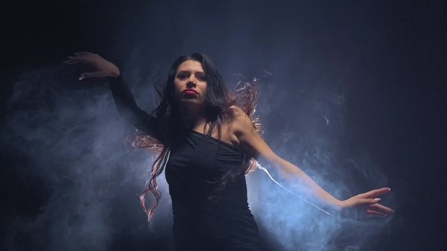 Girl dancing sexy dance with fluttering long hair. Black smoke background. Slow motion