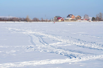 Tracks in the snow from boots, skis and a snowmobile. Frozen lake