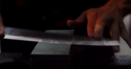 Professional craftsman sharpening Taiwan made Japanese knife blade on wet stone block close up.