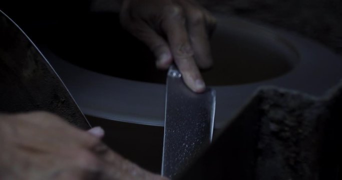 Adult craftsman grinding Taiwan made Japanese sharp knife blade edge on primitive stone wheel.
