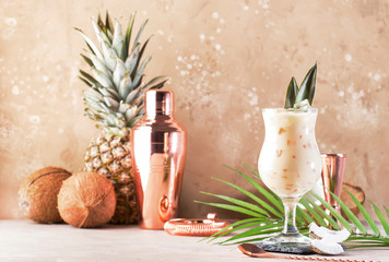 Pina Colada Cocktail on sand beige background with tropical fruits and bar tools, summer relaxation...