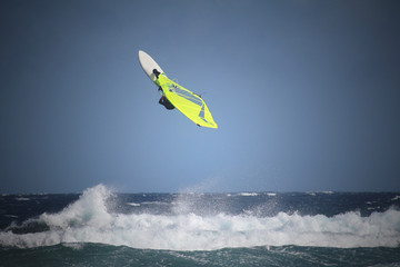 Windsurfer with bright yellow sail looping in the waves of the Atlantic ocean