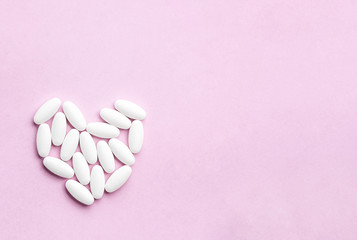 Obraz na płótnie Canvas white heart from tablets and pills isolated on pink background with sunlight.