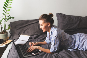 Beautiful young woman working at home in a bed with laptop