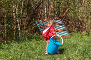 a little girl of two years carries a blue plastic bucket. view of szatsi. summer outdoor recreation with family