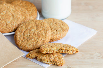 Homemade shortbread cookies made of oatmeal stacked on sackcloth with paper bag and glass bottle of milk on wooden table. Concept food healthy snack for enjoy in holiday.