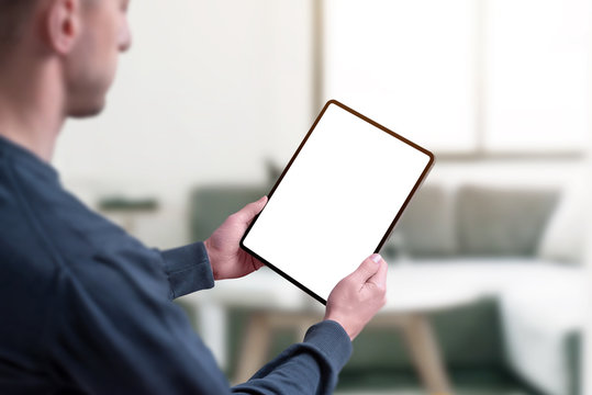 Man Holding Tablet With Isolated Screen In White For Mockup. Living Room Interior In Background