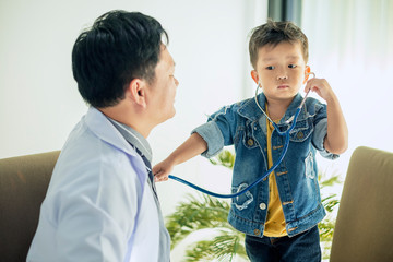 The image of a cute little boy goes to the doctor and is teasing the doctor using a stethoscope to...