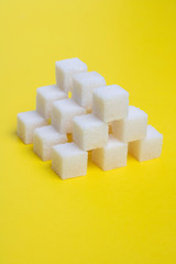 White cubes of shugar on yellow background, vertical food photo