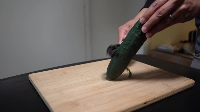 knife chopping cucumber on wooden chopping board medium shot