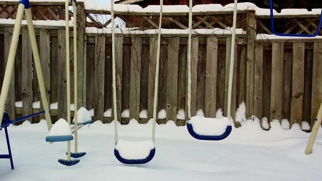 drone zooms in a snowed swingset - snow falling 