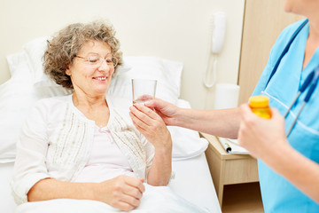 Fototapeta premium Caregiver gives tablets to old woman