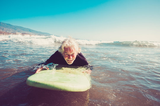 one senior trying surfing alone in the water of the beach and learning surf - mature old man waiting for the waves with his long surfboard