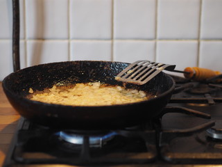 Home cooking. Fried onions in oil in a black pan on the stove. Nearby fried fish. The stage of preparation of the filling for the pie.
