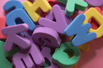 Colorful plastic alphabet letters on pink background, top view