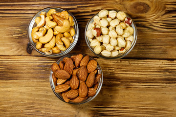 Assortment of nuts on wooden table. Almond, hazelnut and cashew in glass bowls. Top view. Healthy eating concept