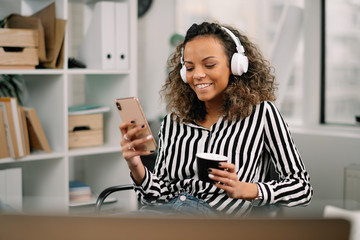 Young african businesswoman in office. Woman listening music and drinking coffee. 