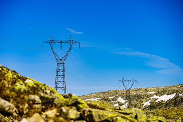 Power line voltage tower in mountains against blue sky
