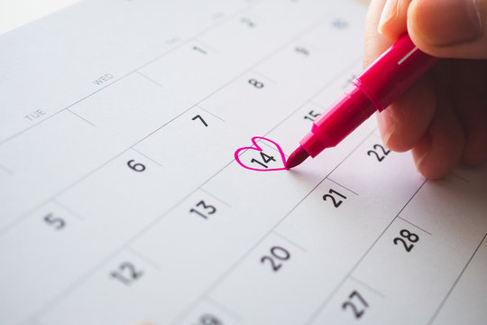 Female Hand with pen mark heart shape on calendar date at 14th valentine day - Powered by Adobe