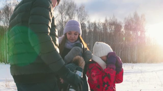 Happy family drinking hot drinks out of the termos outdoors near the winter forest