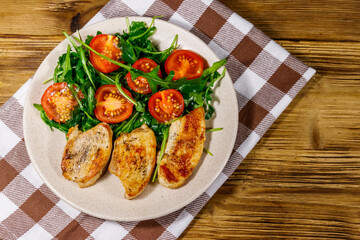 Fried chicken breast with salad of fresh arugula and cherry tomatoes on wooden table. Top view