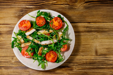 Tasty salad of fried chicken breast, fresh arugula and cherry tomatoes on wooden table. Top view