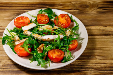 Tasty salad of fried chicken breast, fresh arugula and cherry tomatoes on wooden table