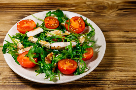 Tasty salad of fried chicken breast, fresh arugula and cherry tomatoes on wooden table