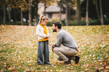 Devilish cute little girl with ponytail standing and looking at her father. Father crouching and...