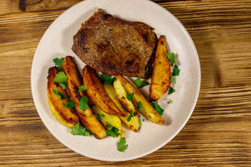 Fried beef steak with potato wedges on wooden table. Top view