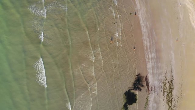 High aerial top down view of waves breaking on beach, people in water, fly over jetty and beach