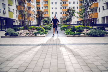 Full length of handsome smiling sportsman with artificial leg standing with hands on hips outdoors surrounded by buildings. Back light.
