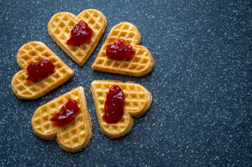 Arrangement of dainty heart-shaped waffles each topped with a dollop of red berry jam a simple stone slab background
