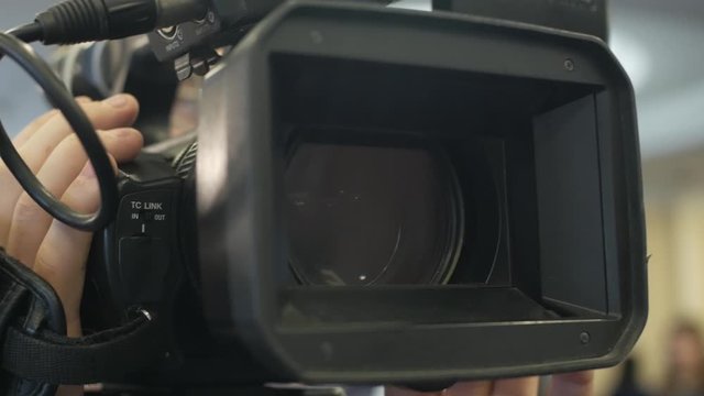 Male hands hold and move a large professional video camera in a close-up view.