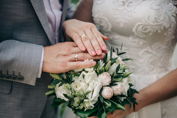 bride and groom put their hands with wedding rings on a bouquet of flowers